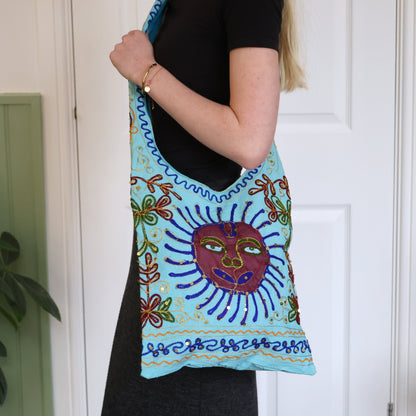 Person holding a colorful bag with a sun design against a white door background