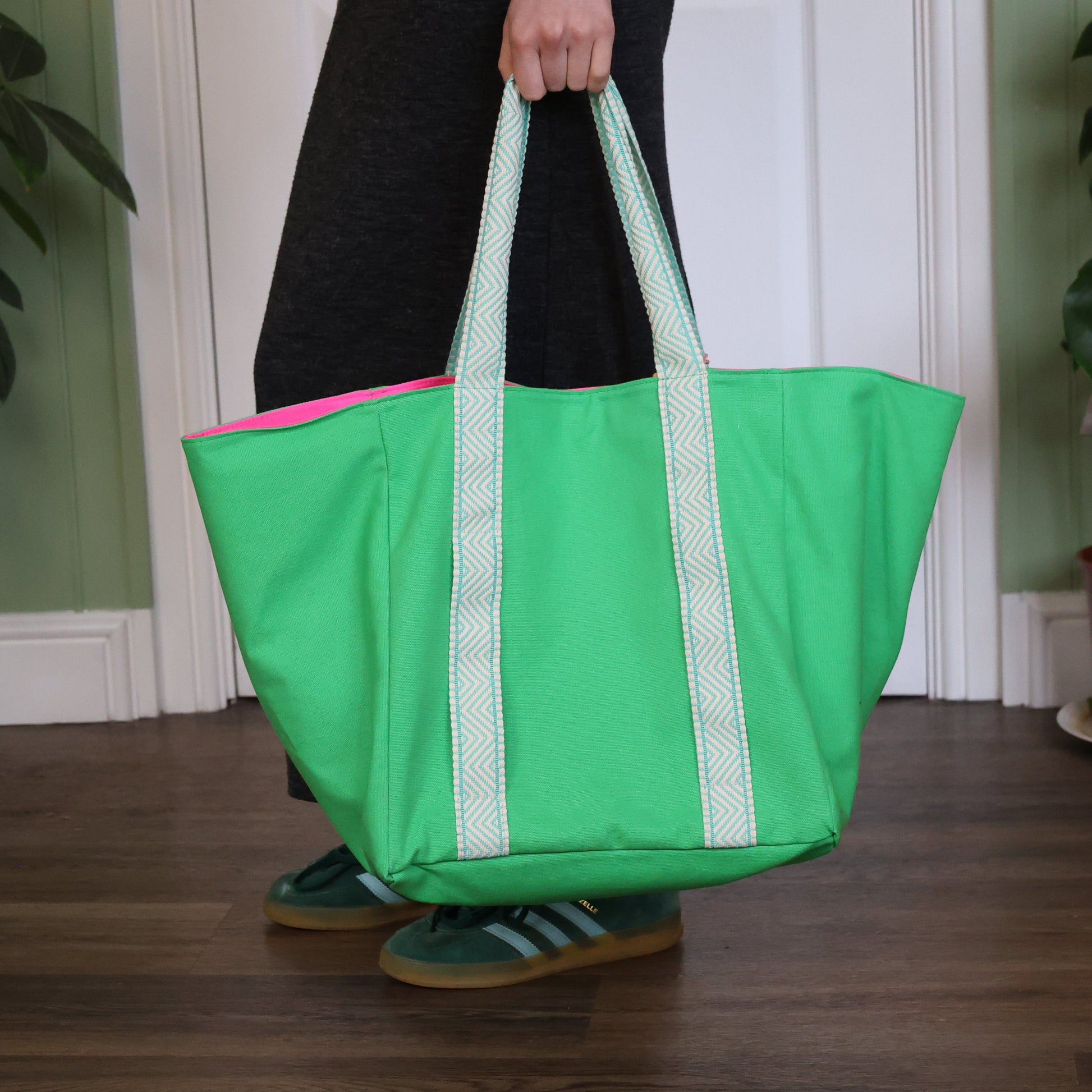 Person holding a green tote bag with a pink interior, standing indoors.