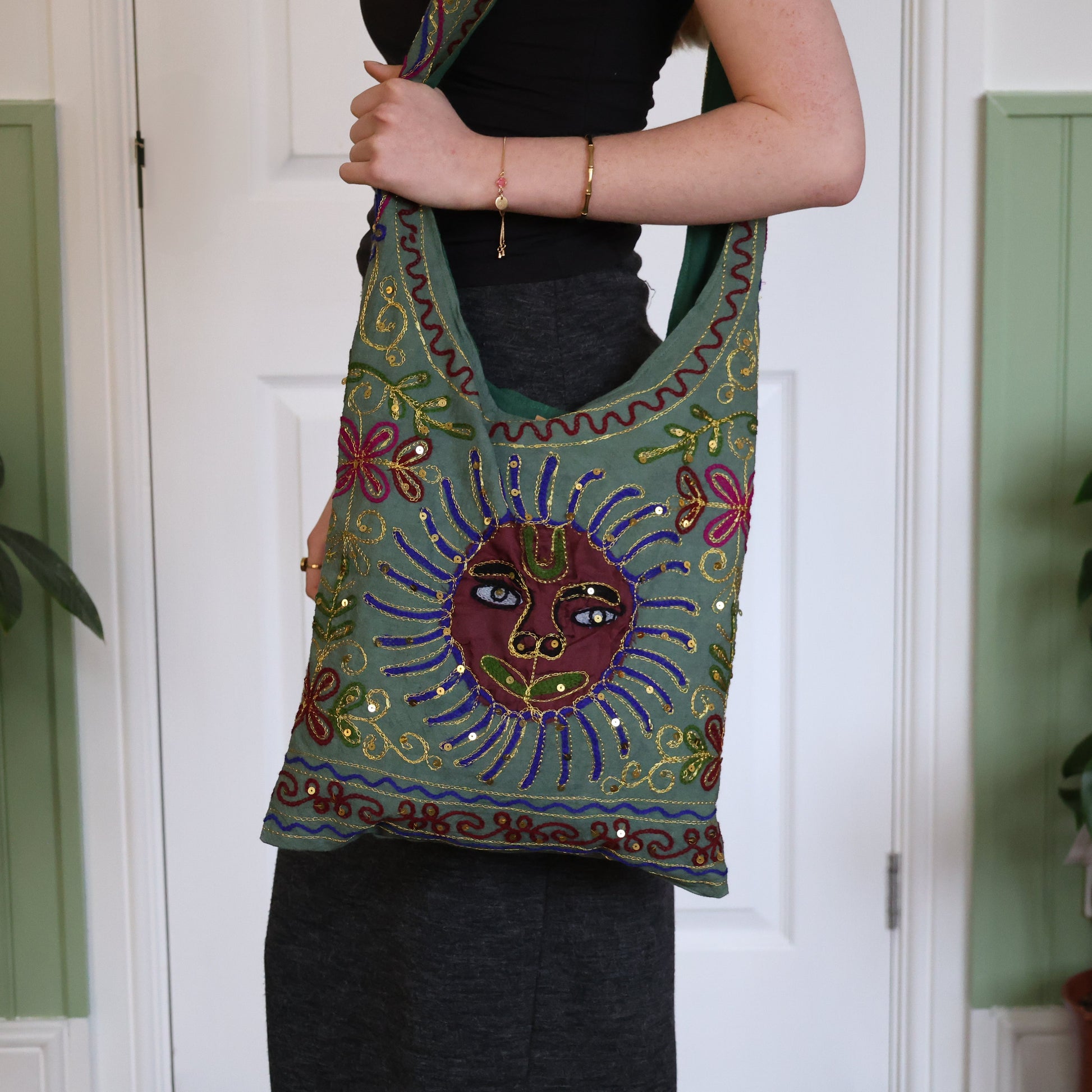 Person holding a colorful embroidered bag with a decorative design against a white door background.