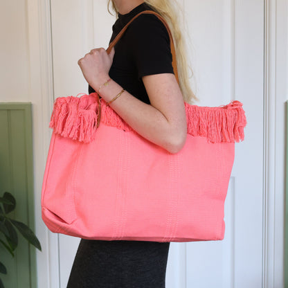 Person holding a pink tote bag with ruffles against a white wall.