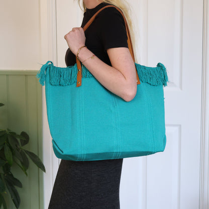 Person holding a teal tote bag with brown handles against a white door background