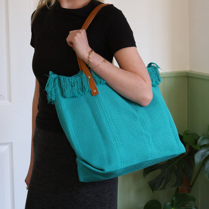 Person holding a teal bag with fringes indoors