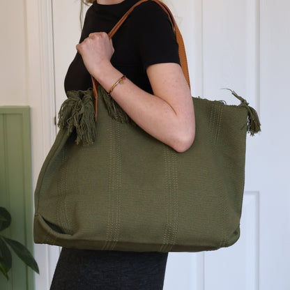 Person holding a green tote bag with fringes against a white door background