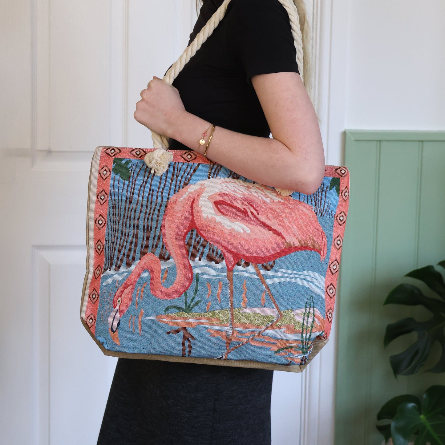 Person holding a tote bag with a flamingo design against a white wall.