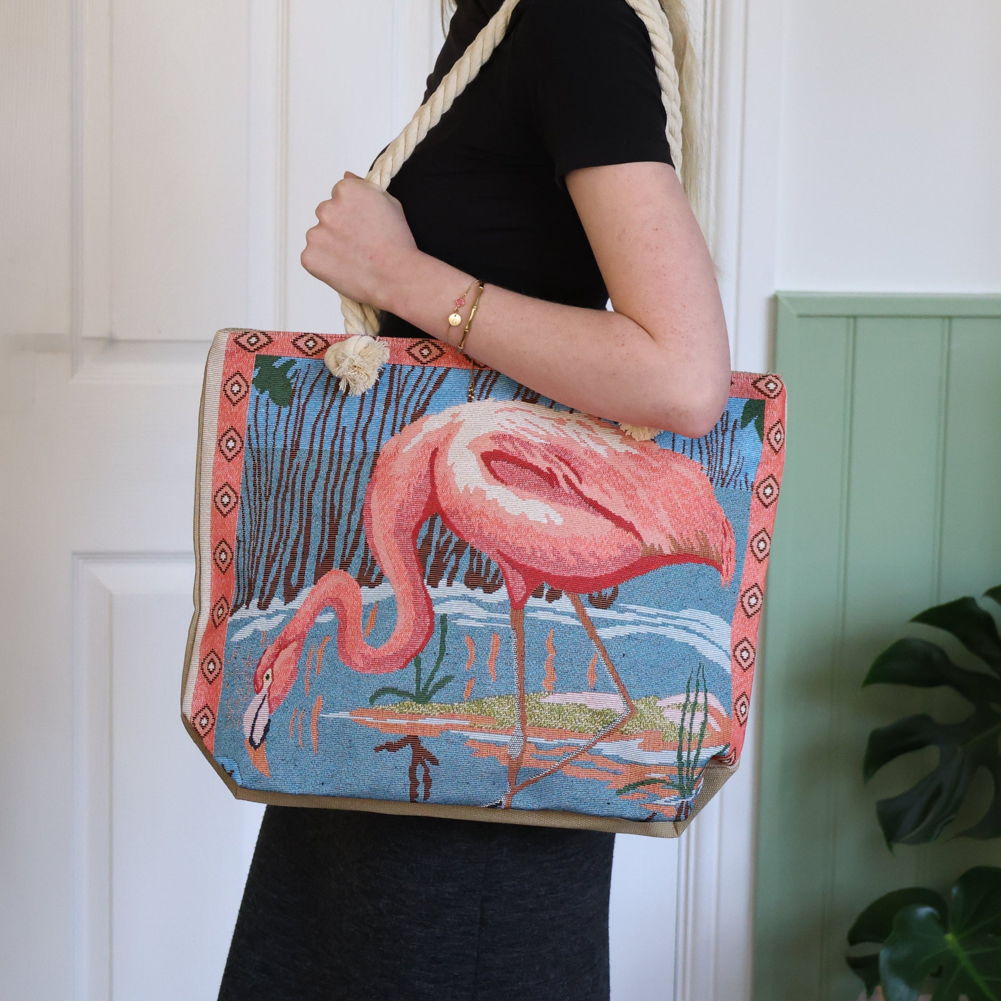 Person holding a tote bag with a flamingo design against a white wall.