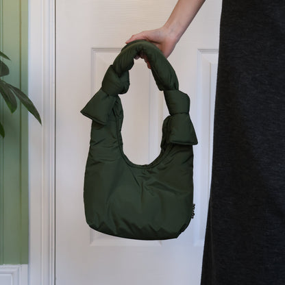 Person holding a green handbag against a white door.