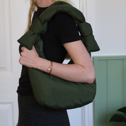 Person wearing a green shoulder bag against a white wall.