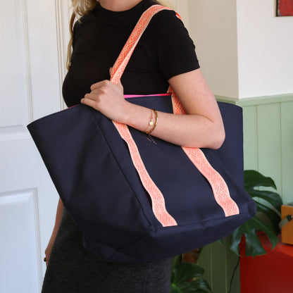 Person holding a navy tote bag with pink straps in a room.
