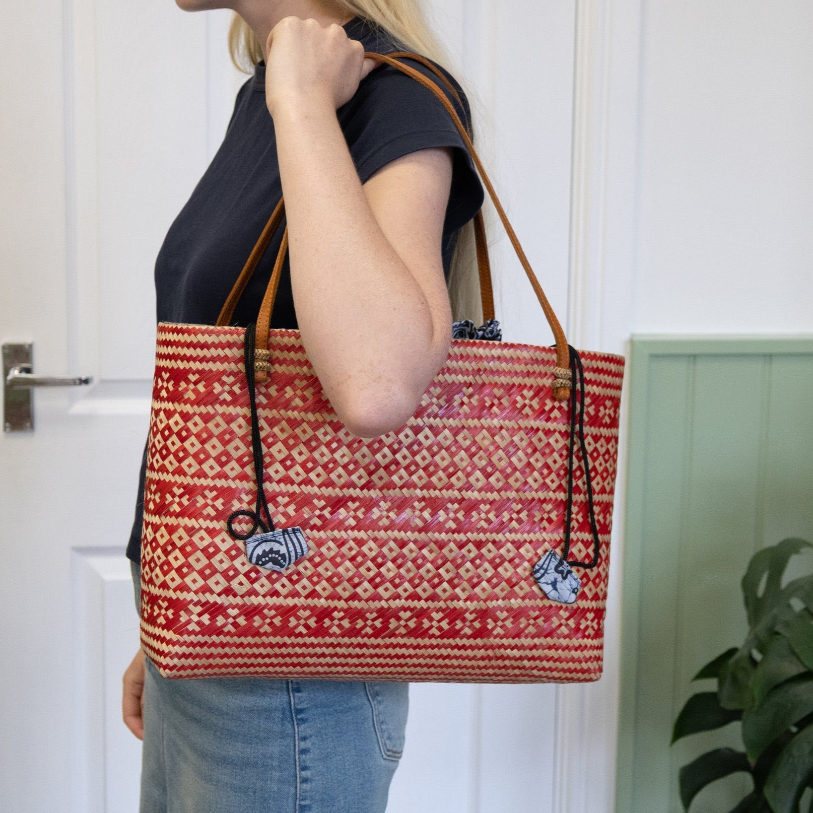 Person holding a red patterned tote bag in front of a white door.