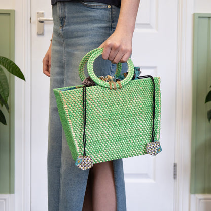 Person holding a green and white patterned handbag indoors.