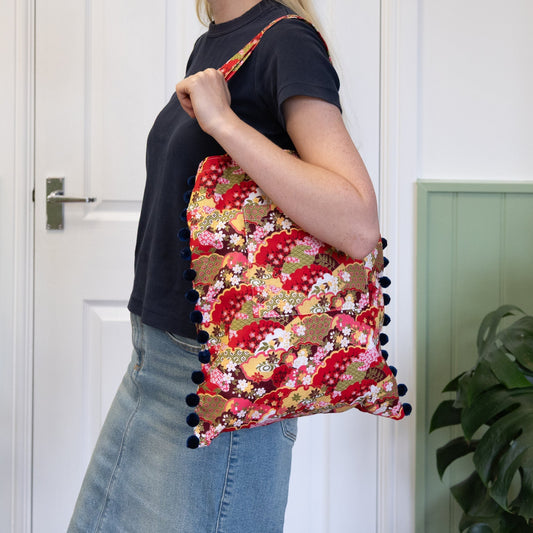 Person holding a red floral bag with pom-poms against a white door background