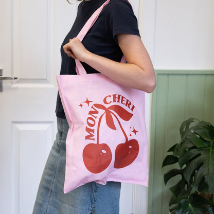 Person holding a pink tote bag with cherry design and text.