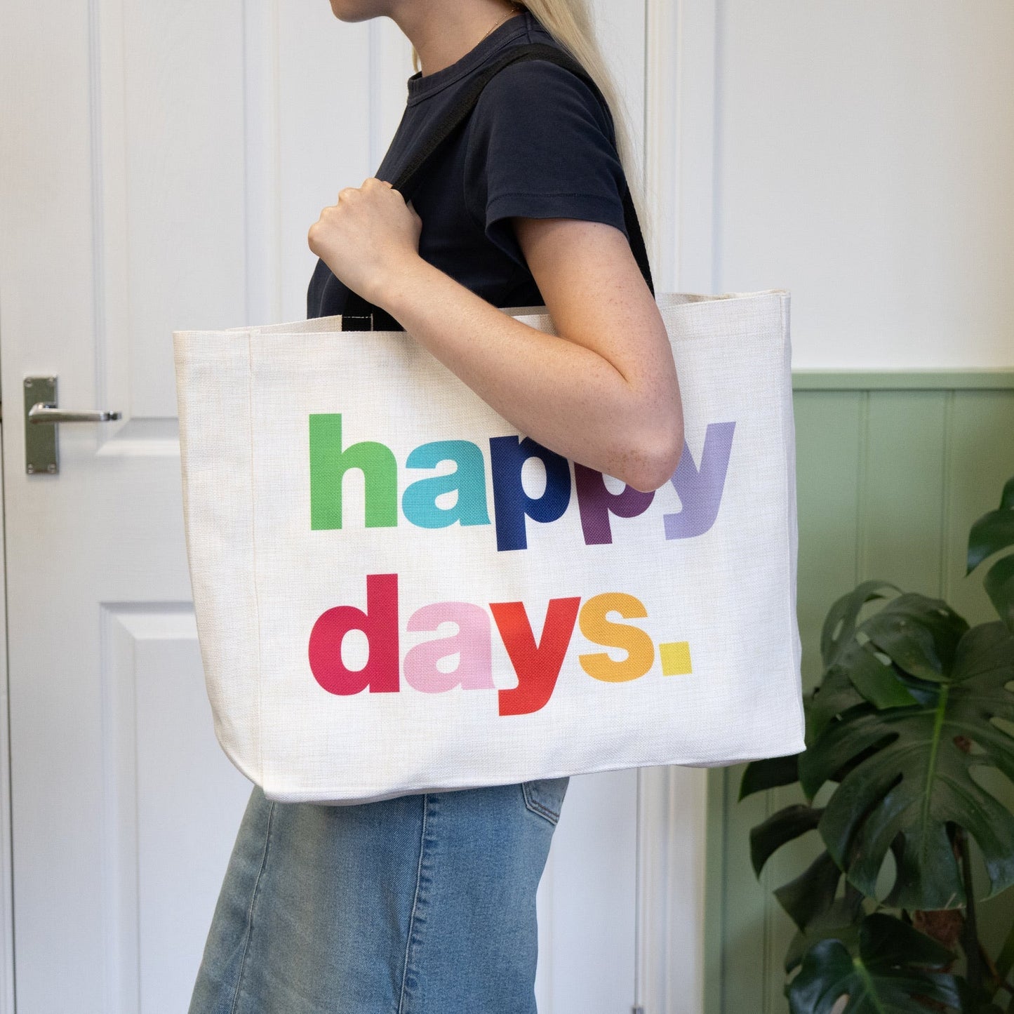 Person holding a tote bag with 'happy days' text in colorful letters.