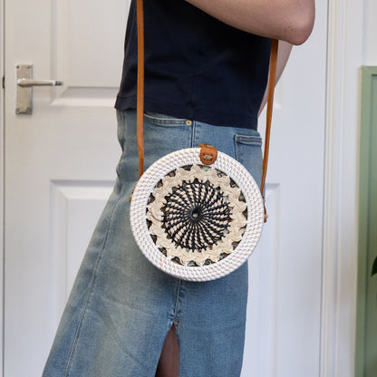Person wearing a round woven bag with a black pattern, standing in a room with a white door and green plant.