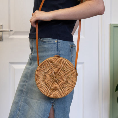 Person holding a round woven bag with a plain background