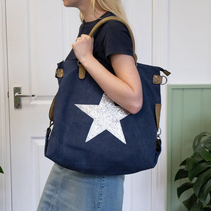 Person holding a navy blue bag with a white star design in a room with plants.