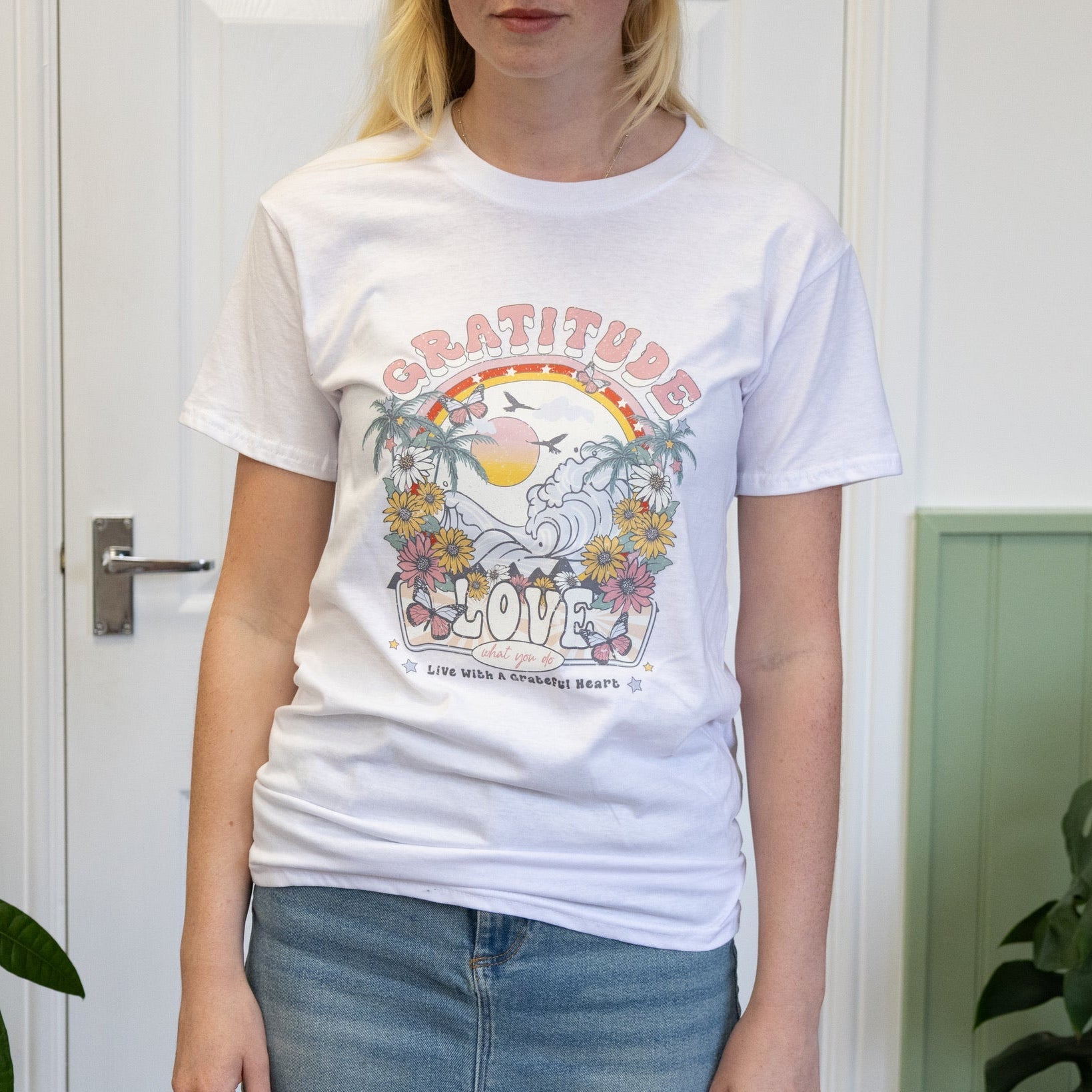 Person wearing a white t-shirt with a graphic design in a room with green plants.