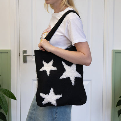 Person holding a black tote bag with white star patterns against a white door background