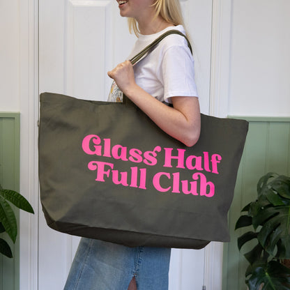 Person holding a tote bag with 'Glass Half Full Club' text in a home setting
