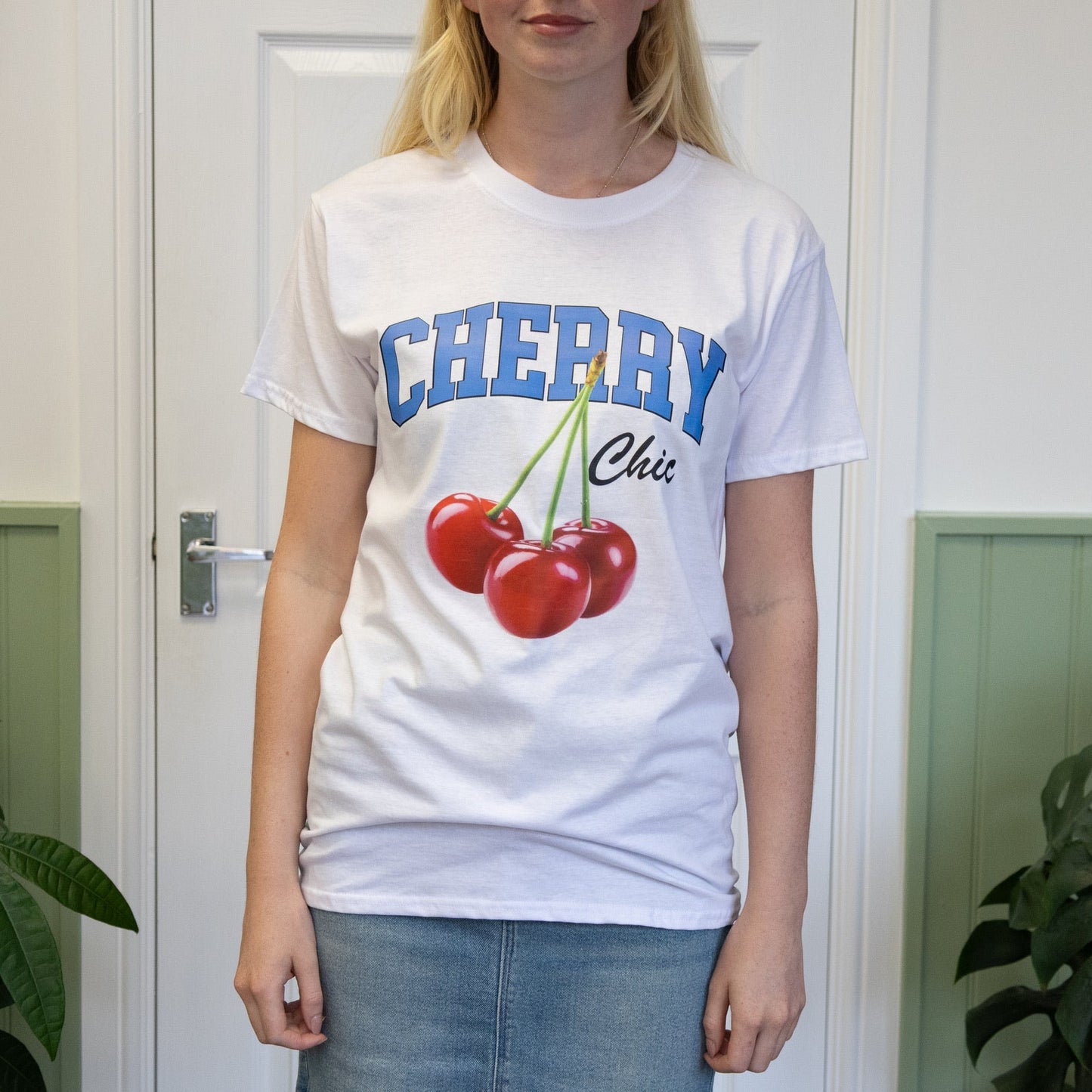 Person wearing a white t-shirt with 'Cherry' design and text in a room with plants.