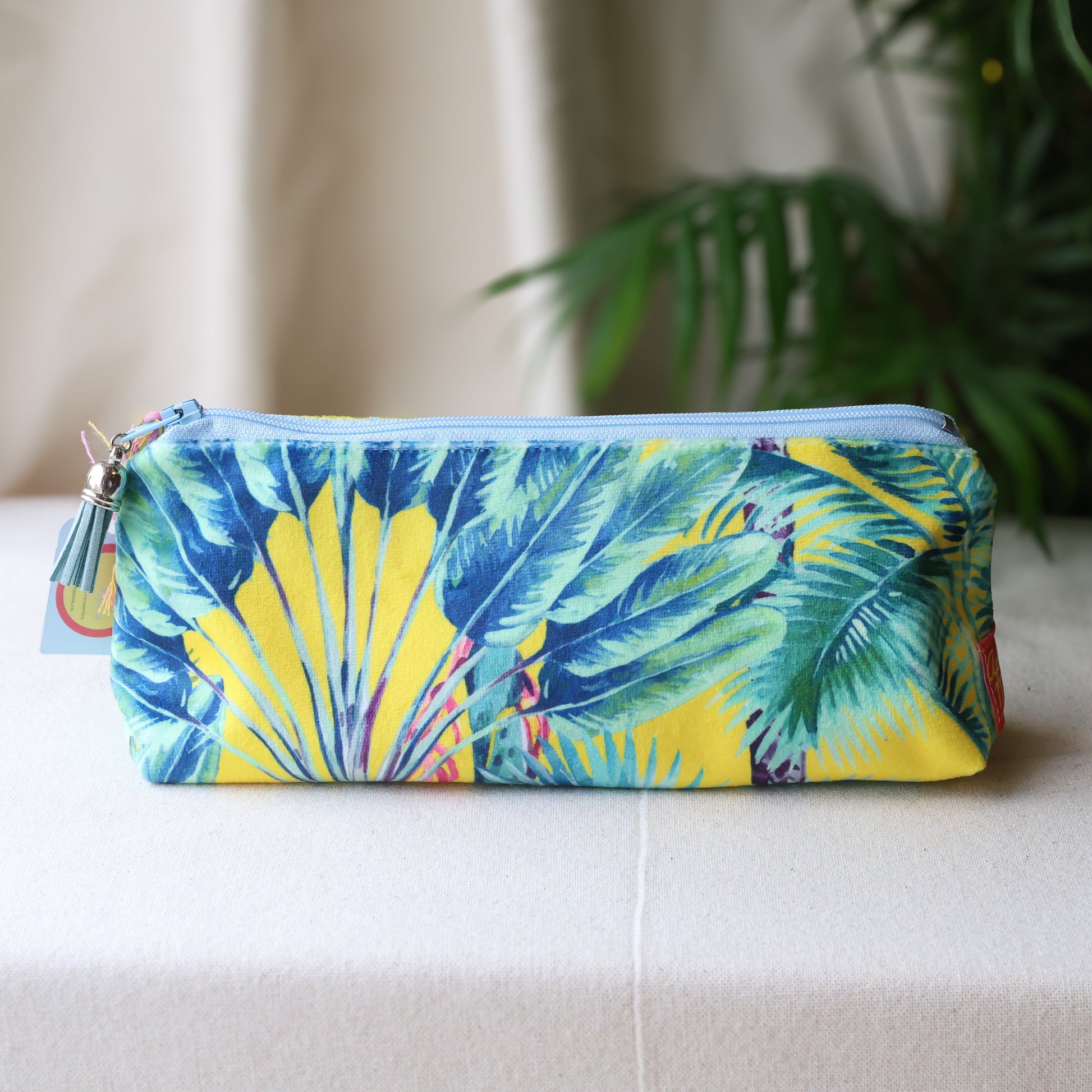 Tropical leaf patterned pouch on a white surface with a plant in the background