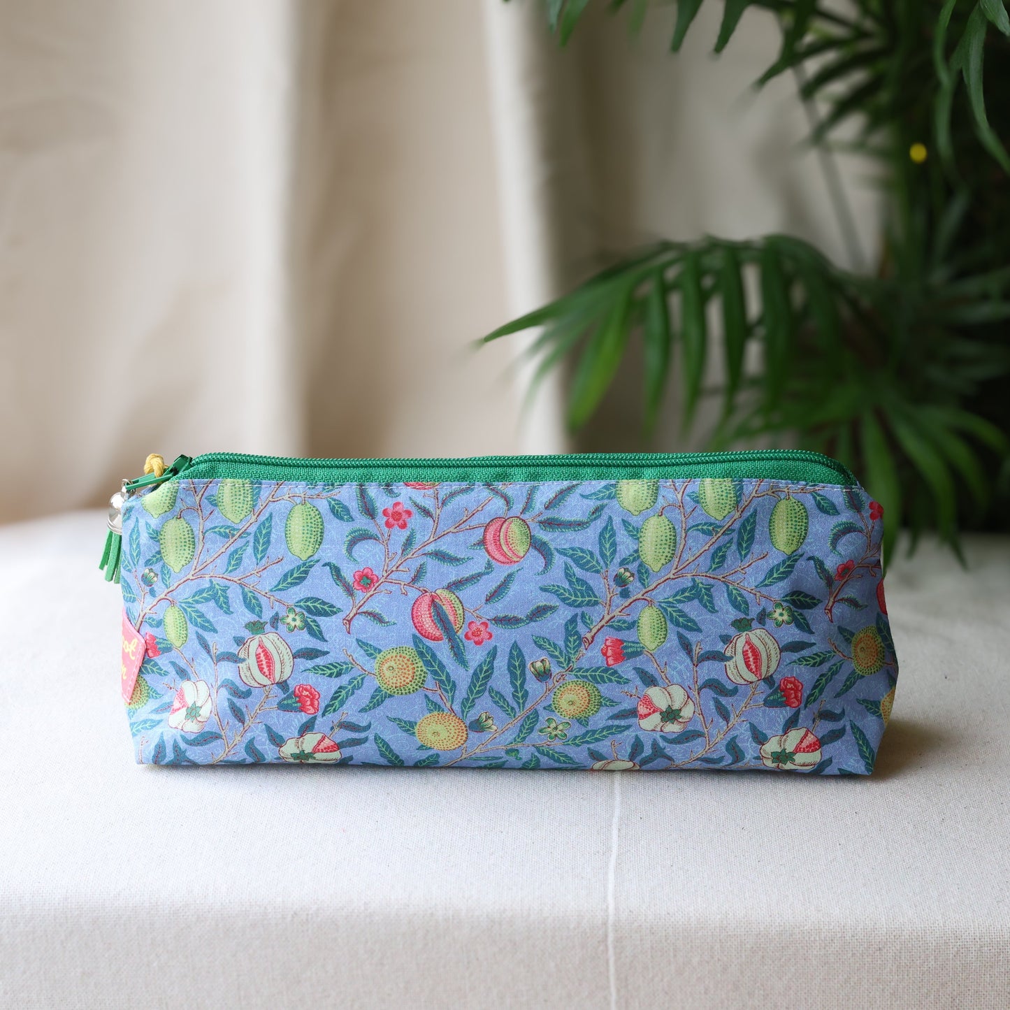 Floral patterned pouch with a green zipper on a white surface with a plant in the background