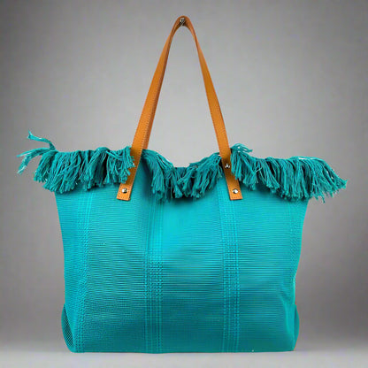 Turquoise tote bag with frayed edges and brown handles on a gray background