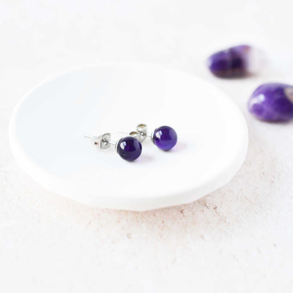 Purple gemstone stud earrings on a white plate with a marble background