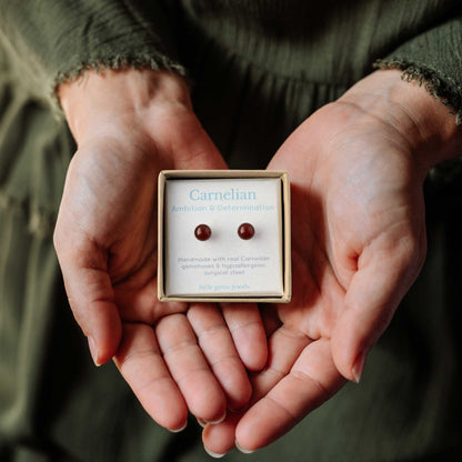 Hands holding small square eco friendly gift box containing Carnelian gemstone ball stud earrings.