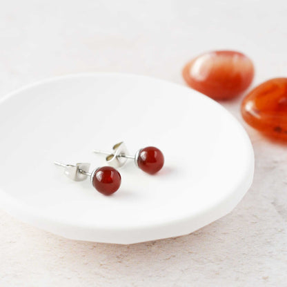 Orange gemstone ball stud earrings laying in white trinket dish.