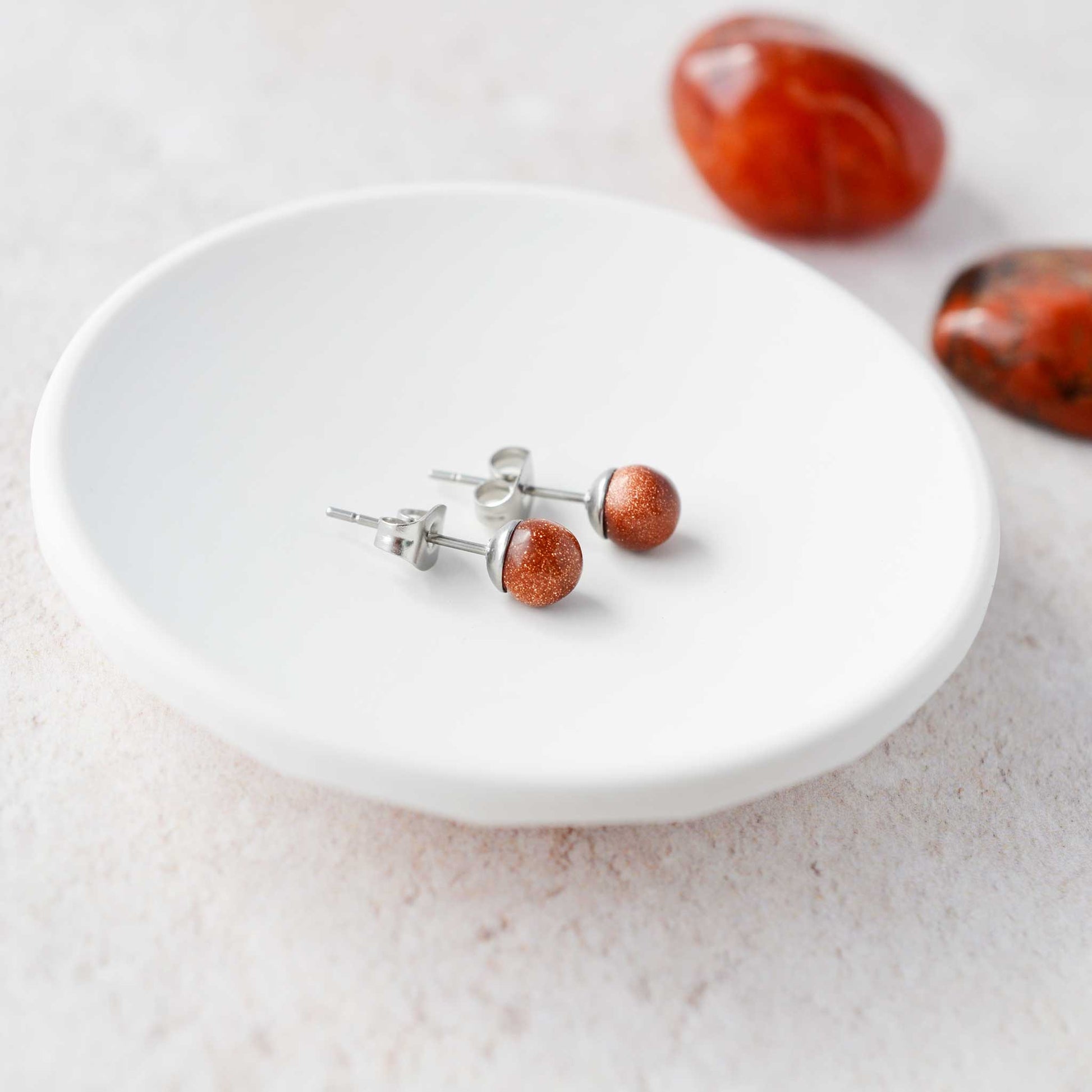 Goldstone round stone earrings laying in white trinket dish.