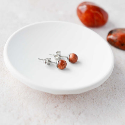 Goldstone round stone earrings laying in white trinket dish.