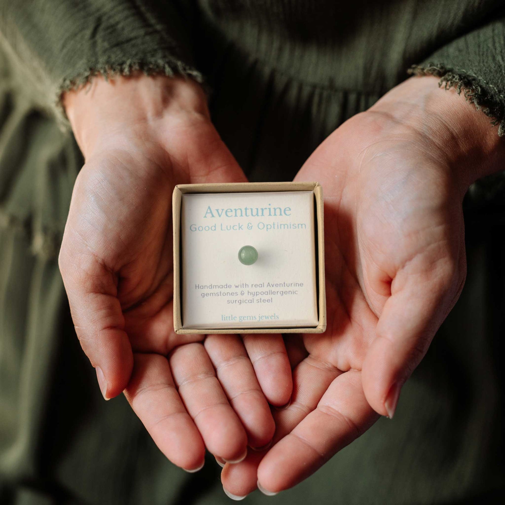 Woman wearing green dress holding gift box in hands containing single green aventurine stud earring.