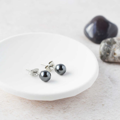 Dark grey Hematite ball stud earrings laying in white trinket dish.