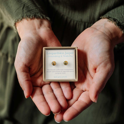 Hands holding small square eco friendly gift box containing Leopardskin Jasper gemstone ball stud earrings.