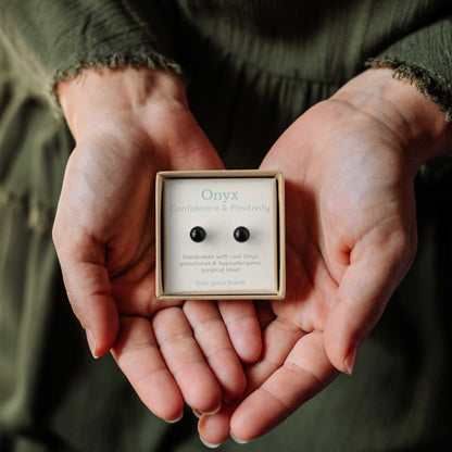 Hands holding small square eco friendly gft box containing Onyx gemstone ball stud earrings.