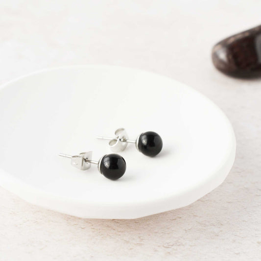 Black Onyx gemstone ball stud earrings laying in white trinket dish.