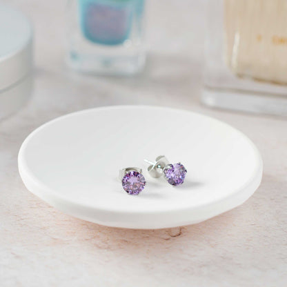 Purple stud earrings on a white round dish with a blurred background