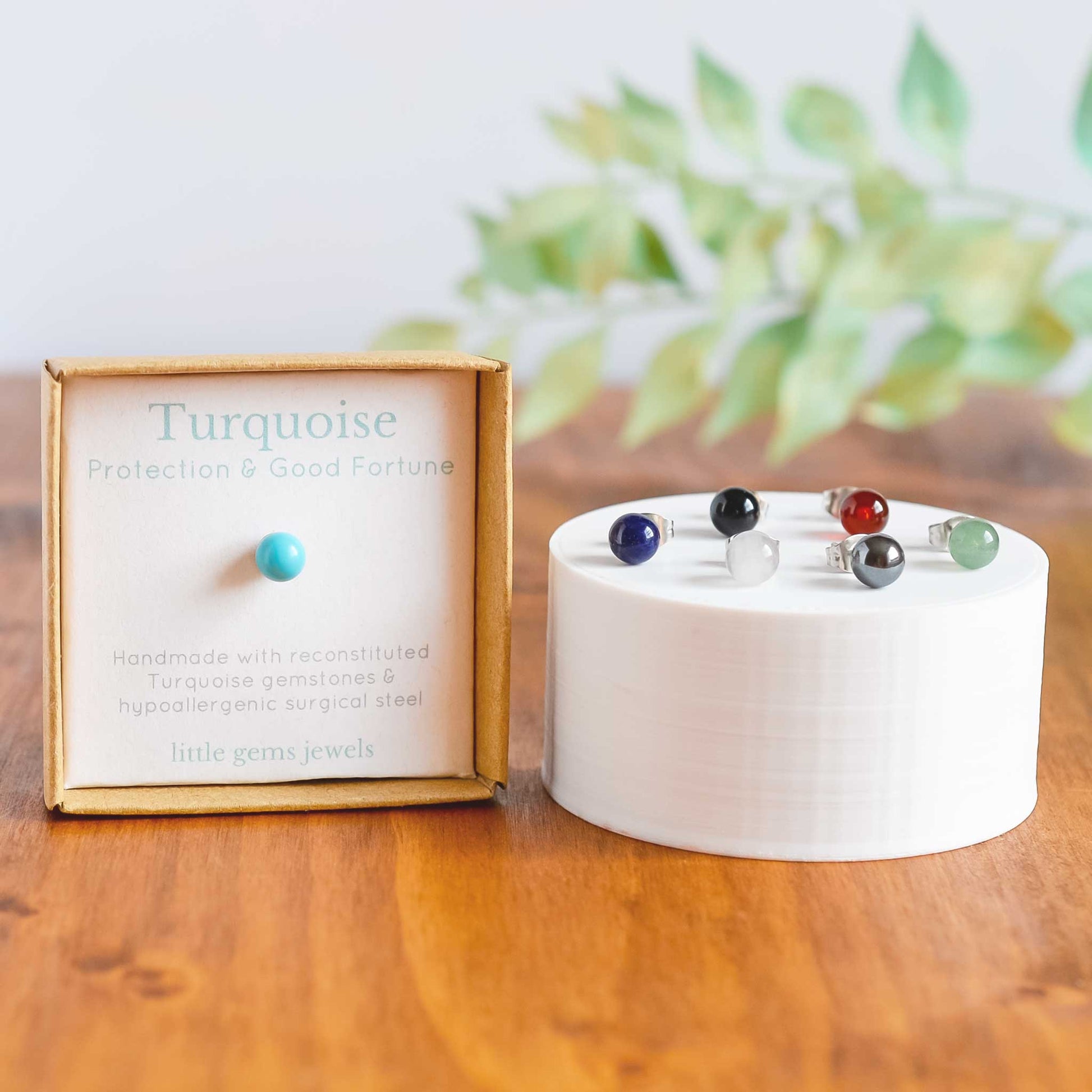 Turquoise single stud in gift box next to six other gemstone studs on white display plinth.