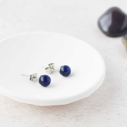 Dark blue gemstone ball stud earrings laying in white trinket dish.