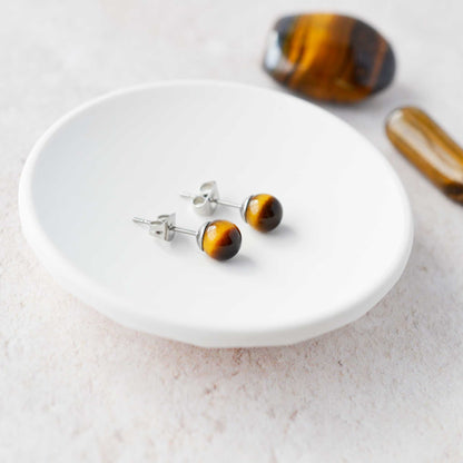 Tiger's Eye ball stud earrings laying in a white trinket dish.