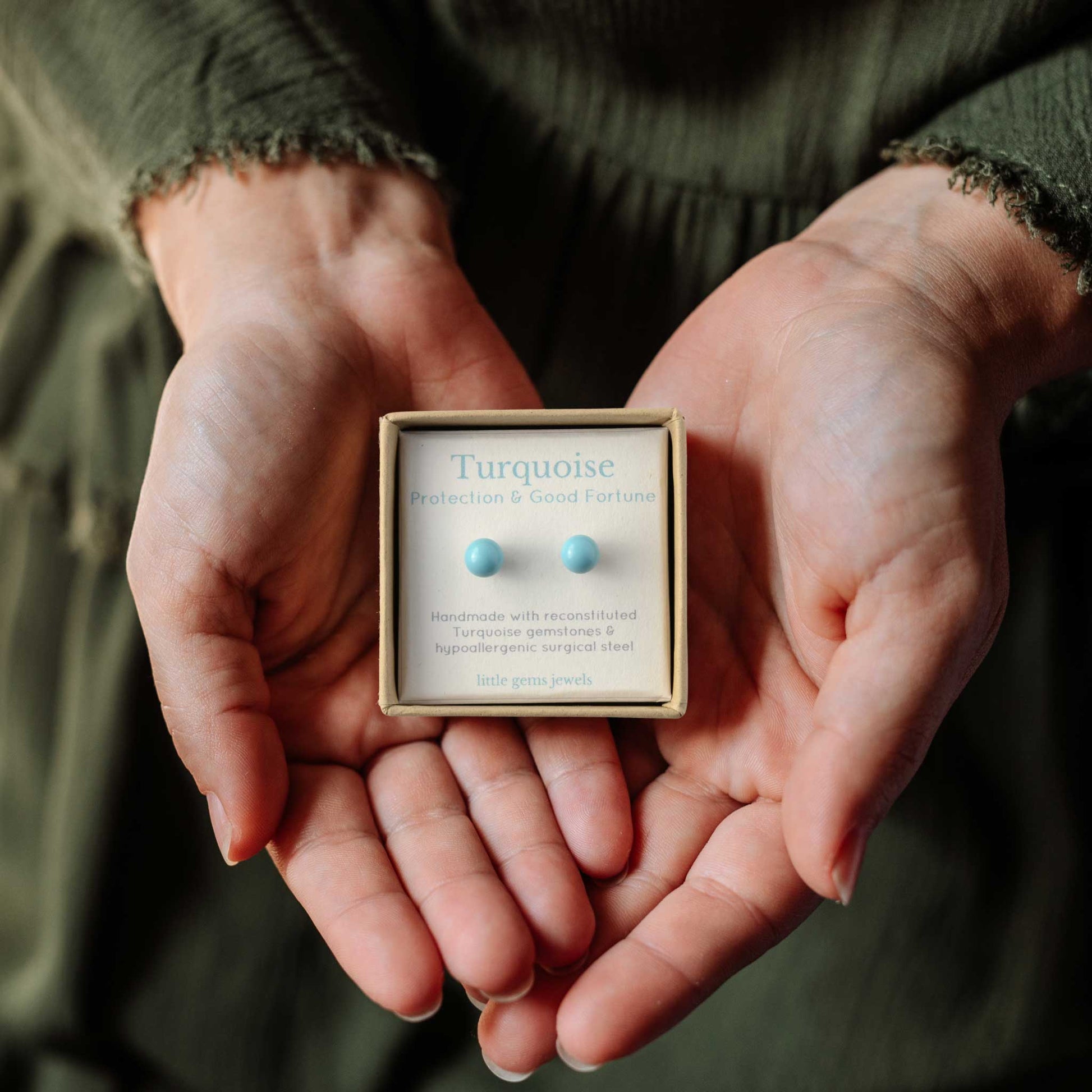 Hands holds small square eco friendly gift box containing Turquoise gemstone ball stud earrings.