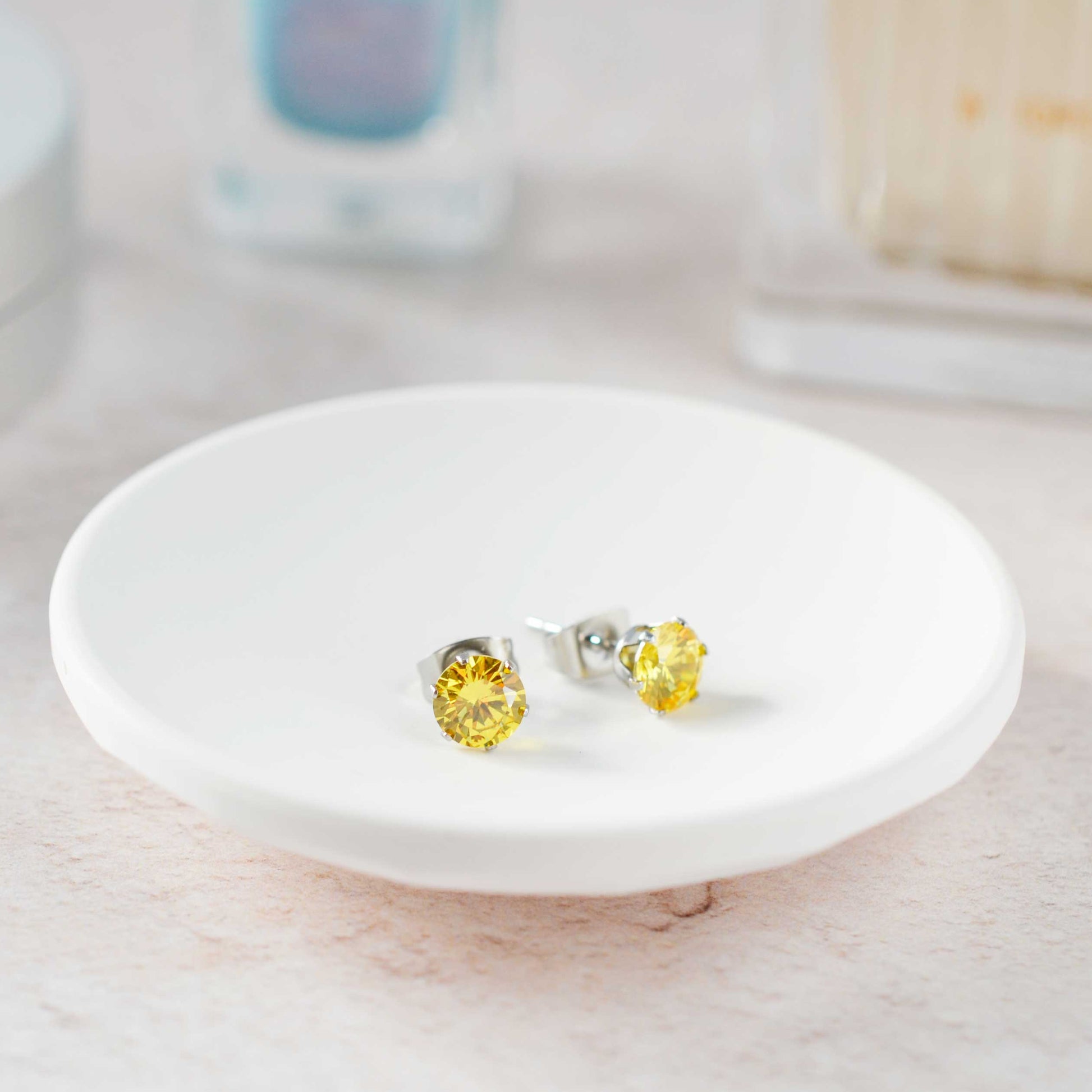 Yellow gemstone stud earrings on a white dish with a blurred background