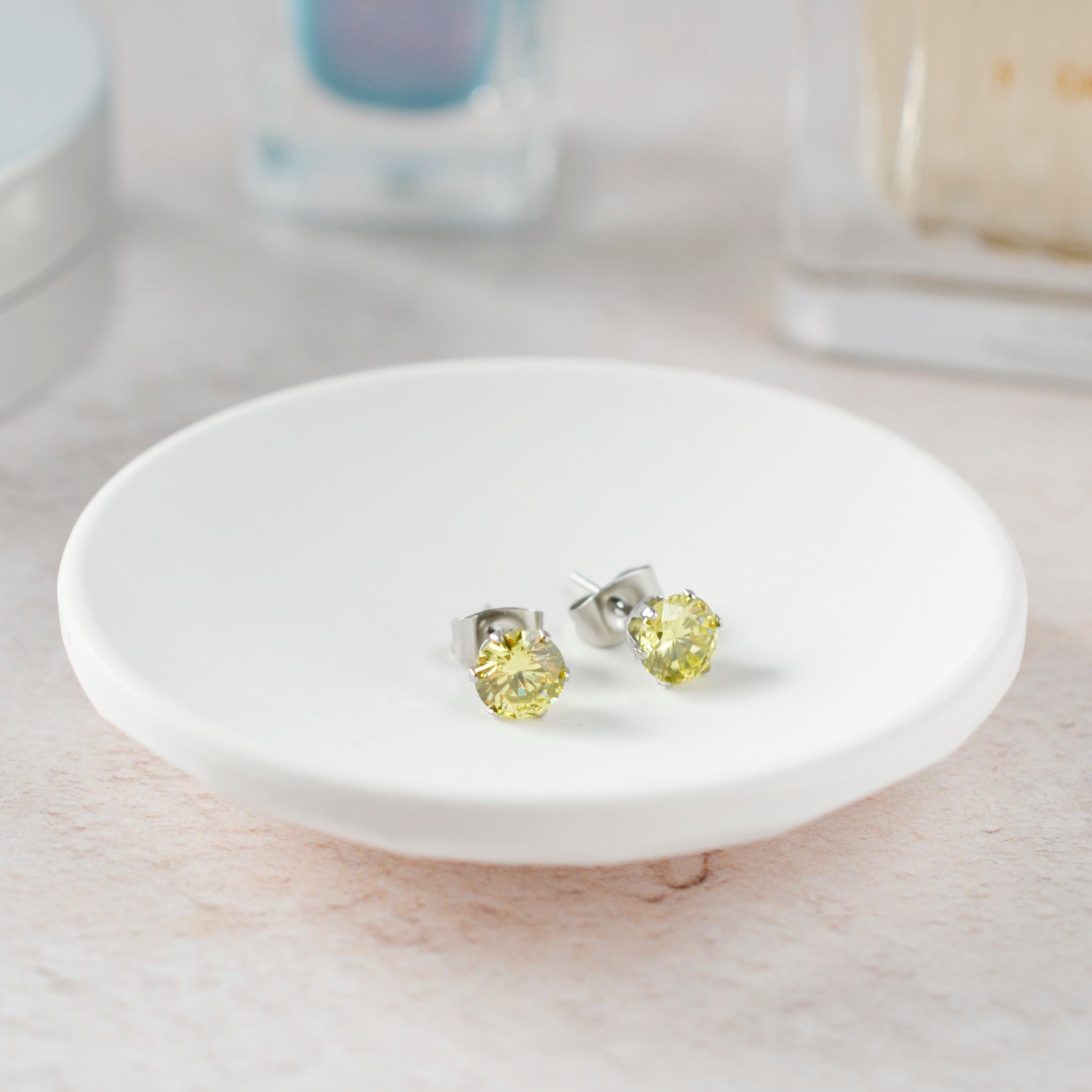 Green gemstone stud earrings on a white ceramic dish with a blurred background