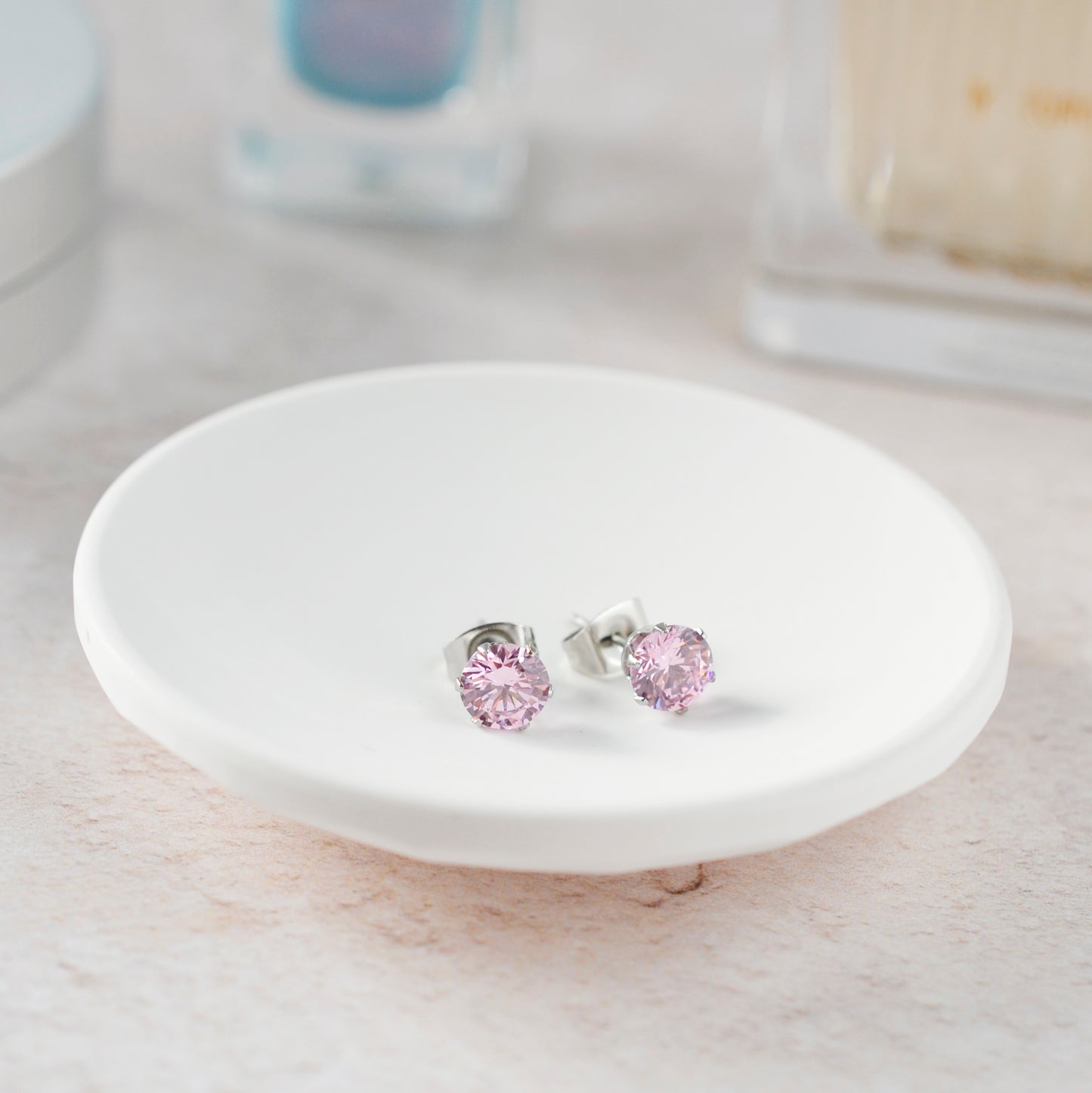 Pink stud earrings on a white ceramic dish with a blurred background