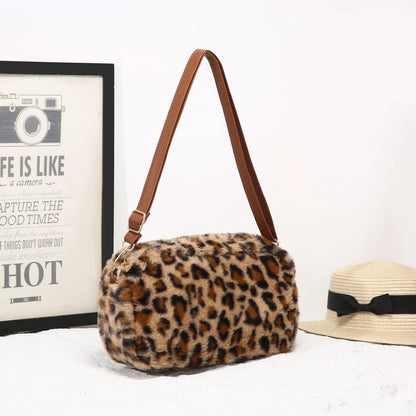 Leopard print handbag with brown strap on a white surface next to a framed picture and straw hat.