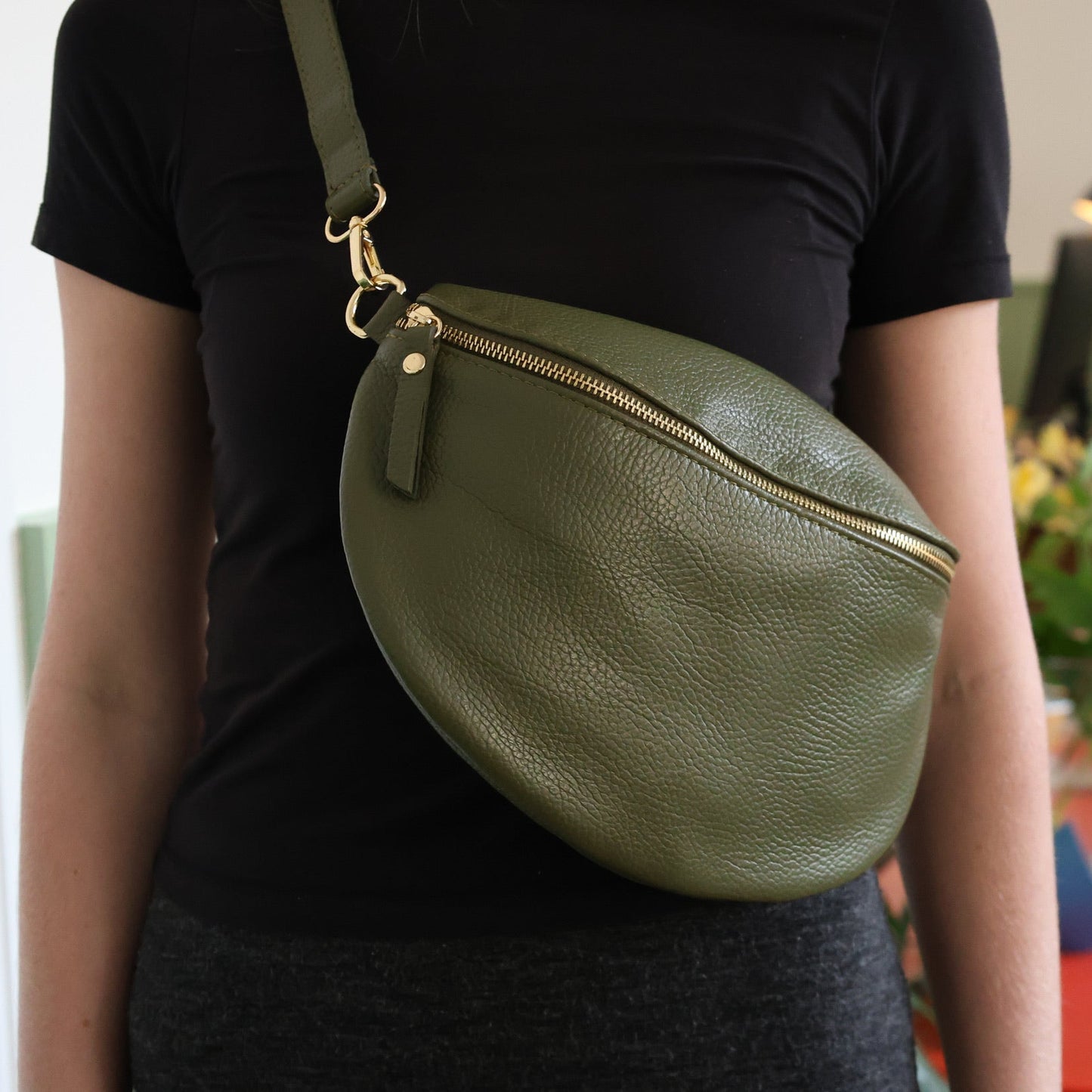 Person wearing a green leather crossbody bag indoors