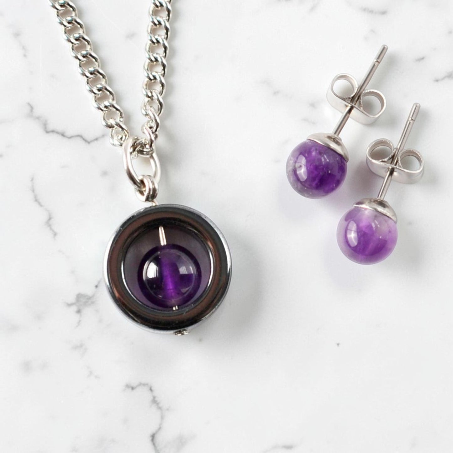 Amethyst necklace and stud earring set laying on marble background.