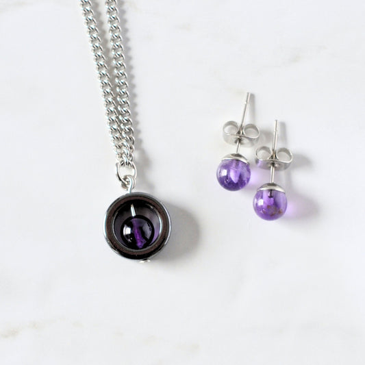 Amethyst spinner necklace and stud earrings laying on a white marble background.