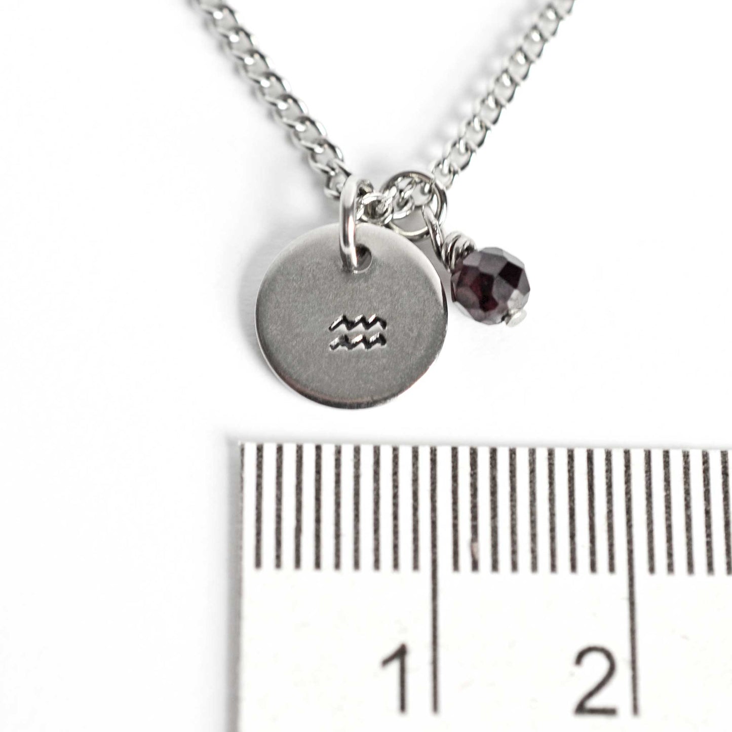 1cm diameter disc pendant with hand stamped Aquarius zodiac sign and 4mm Garnet gemstone charm